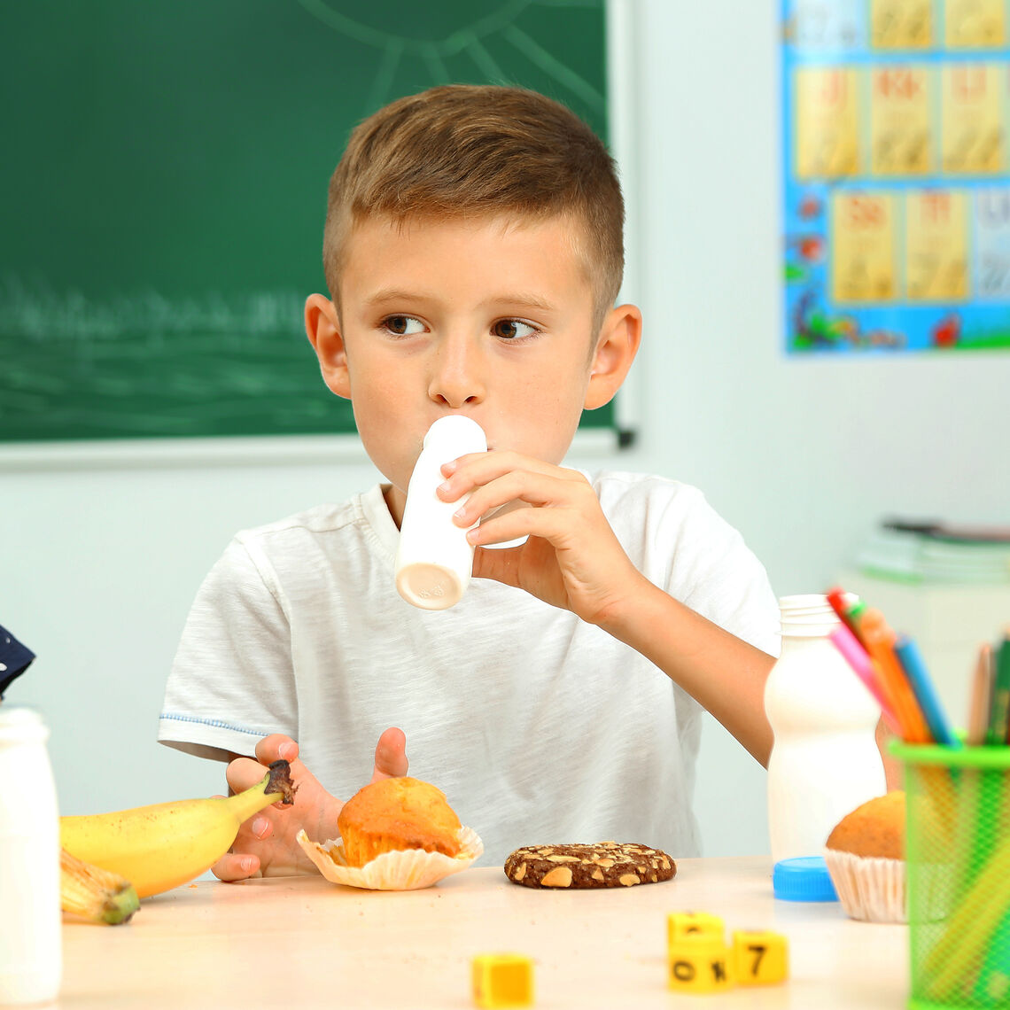 a boy sips milk with a muffin at his desk in the classroom